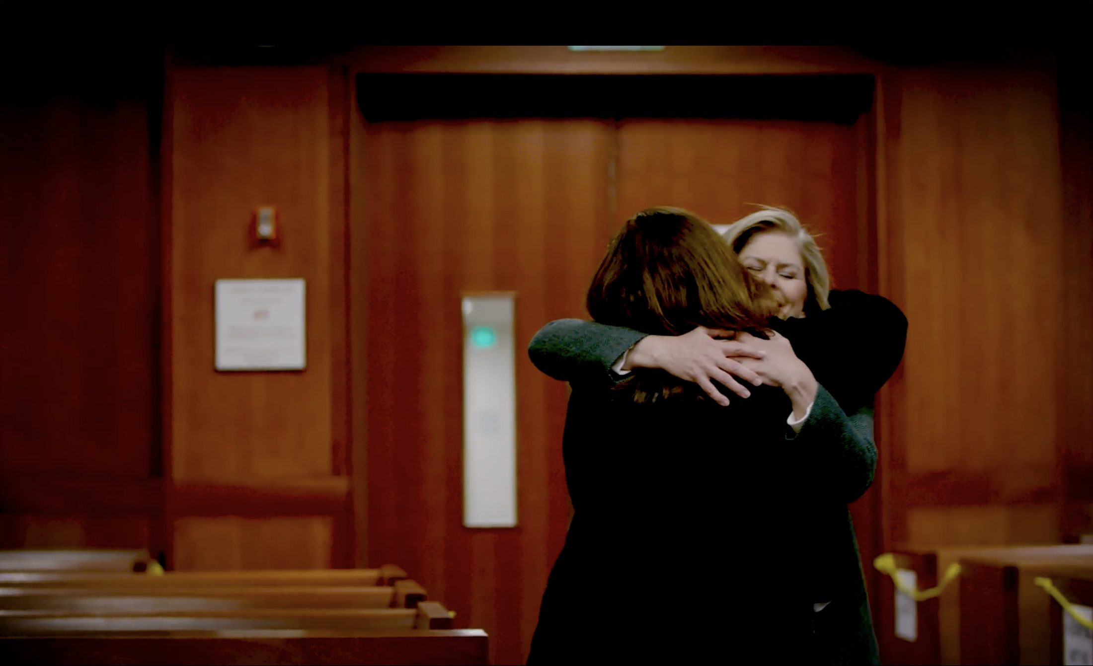 Two women embrace in a wood-paneled courtroom — a still from The Last Trace.